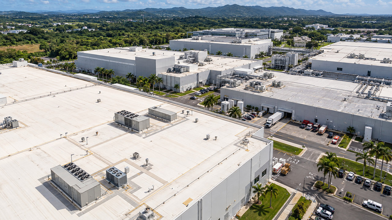 Vista aérea de un campus farmacéutico con techos blancos, palmas y montañas en Puerto Rico